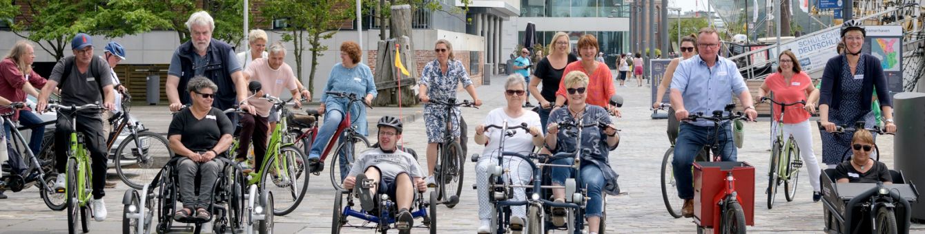 Menschen auf unterschiedlichen Fahrrädern fahren nebeneinander am Neuen Hafen in Bremerhaven entlang. Auch Inklusionsfahrräder für unterschiedliche Beeinträchtigungen sind dabei.