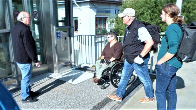 Zwei Fußgänger und eine Fußgängerin und eine Frau im Rollstuhl betrachten den Fahrstuhl am Bahnhof Wulsdorf