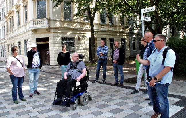 eine Gruppe von Menschen auf einem öffentlichen Platz, einer der Menschen sitzt in einem Rollstuhl