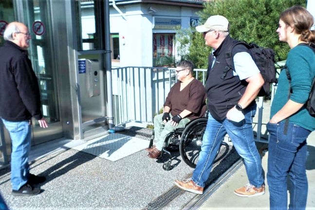 Zwei Fußgänger und eine Fußgängerin und eine Frau im Rollstuhl betrachten den Fahrstuhl am Bahnhof Wulsdorf